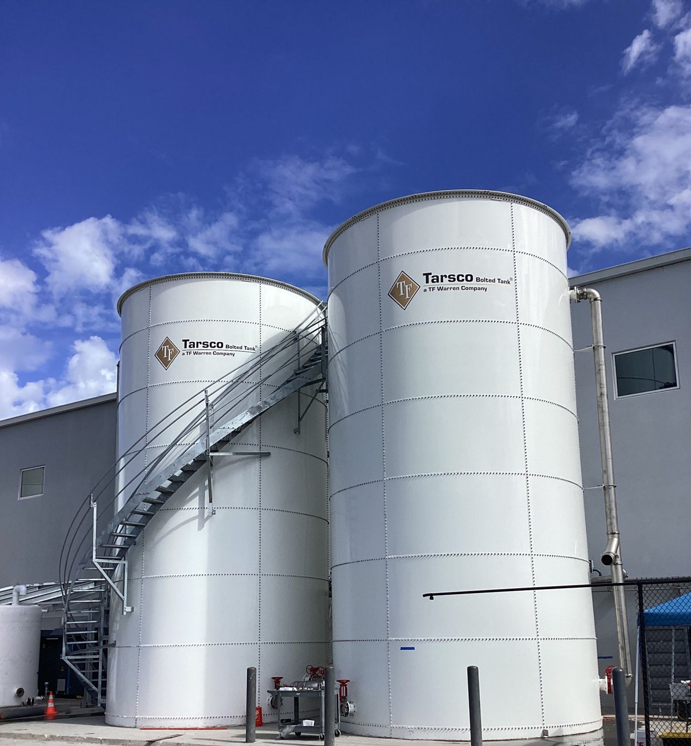 The image shows two large bolted storage tanks manufactured by Tarsco Bolted Tank, a TF Warren Company.