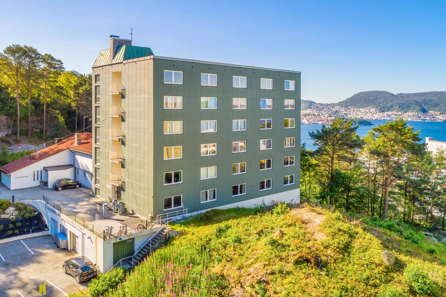 The facade of Øyjordsveien student housing, with the sea in the background, surrounded by green areas and parking facilities.