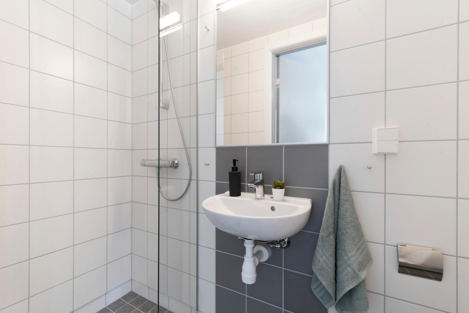 Bathroom with shower, wall-mounted sink, mirror, and grey and white tiled walls