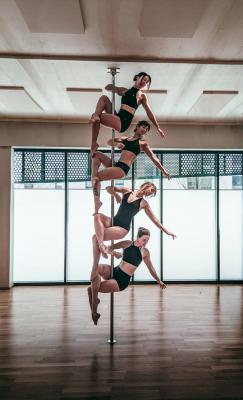 Four pole dancers holding different poses on the same pole in a bright studio