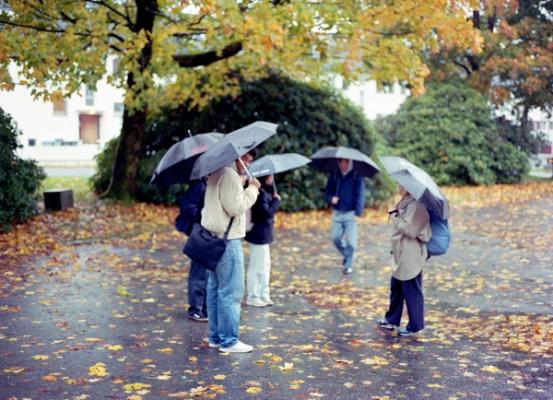 En gruppe studenter står i regnet og holder paraplyer for å beskytte seg mot regnskuret.