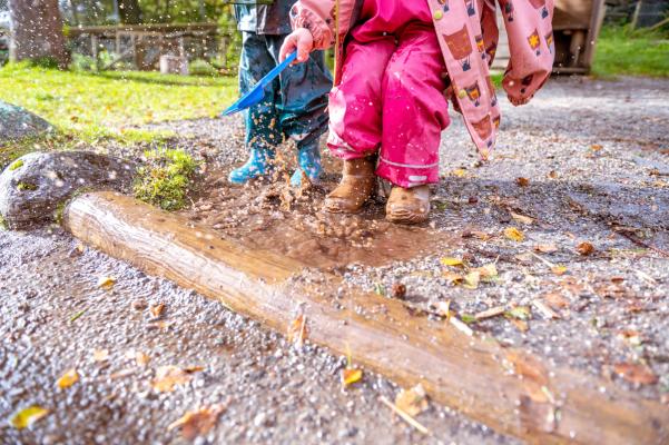Two children in colorful rain gear playing in a puddle.