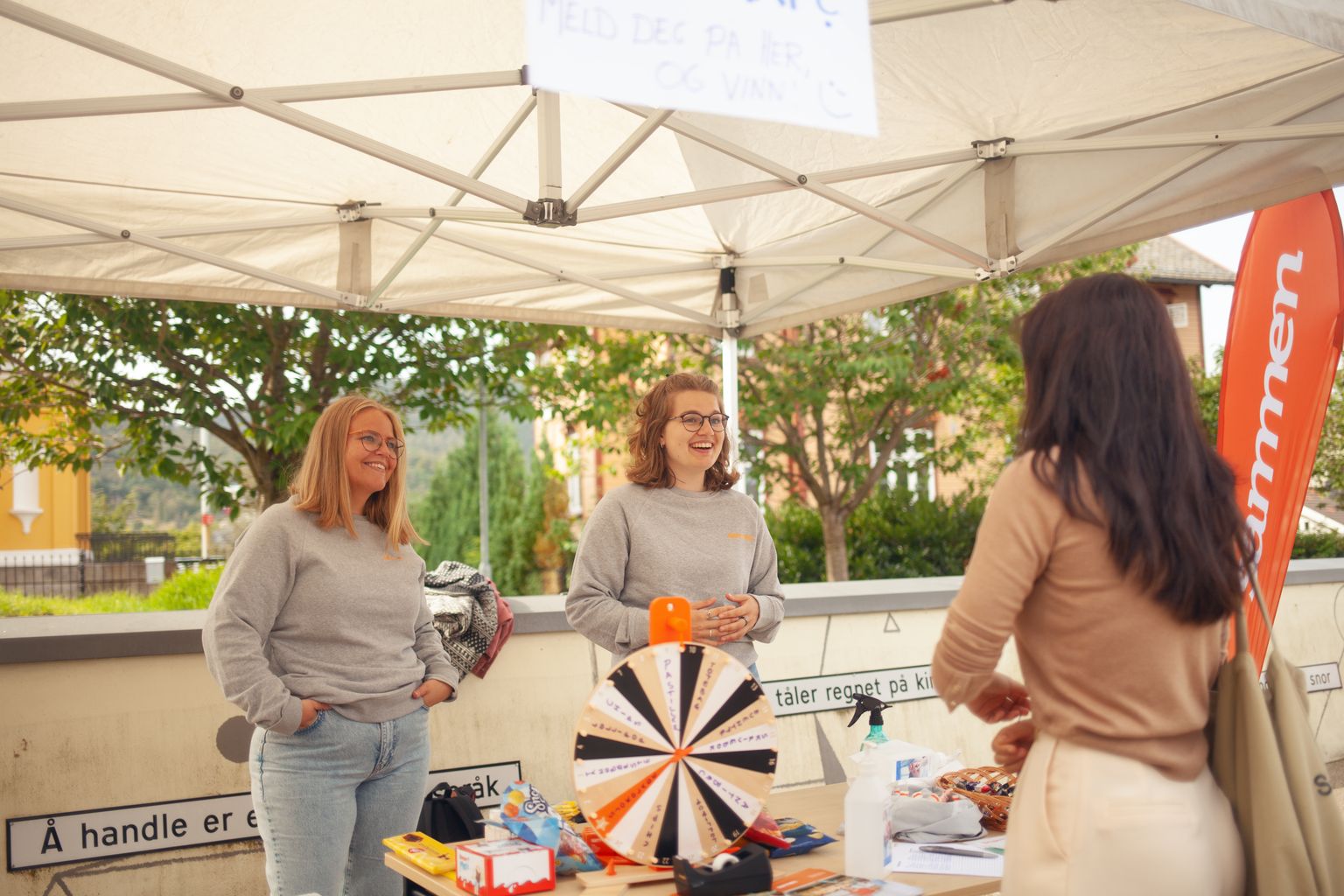 En glad gruppe studenter står ved en stand med et lykkehjul, deler smil og forventning.