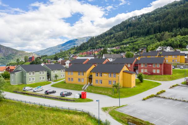 Picture of our houses at Elvatunet: Colorful buildings with green surroundings and parking spaces around.