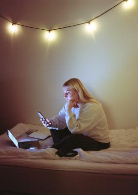 A female student sitting in bed with a laptop and a mobile phone.