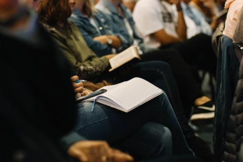 En gruppe mennesker som sitter på en konferanse, aktivt deltar og tar notater.