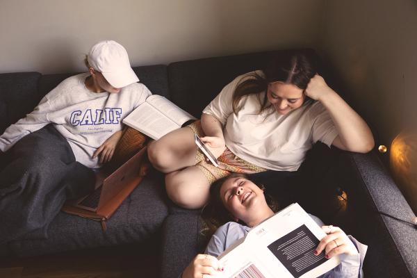 Three women sitting on a couch, engrossed in books. A cozy reading session filled with knowledge and relaxation.