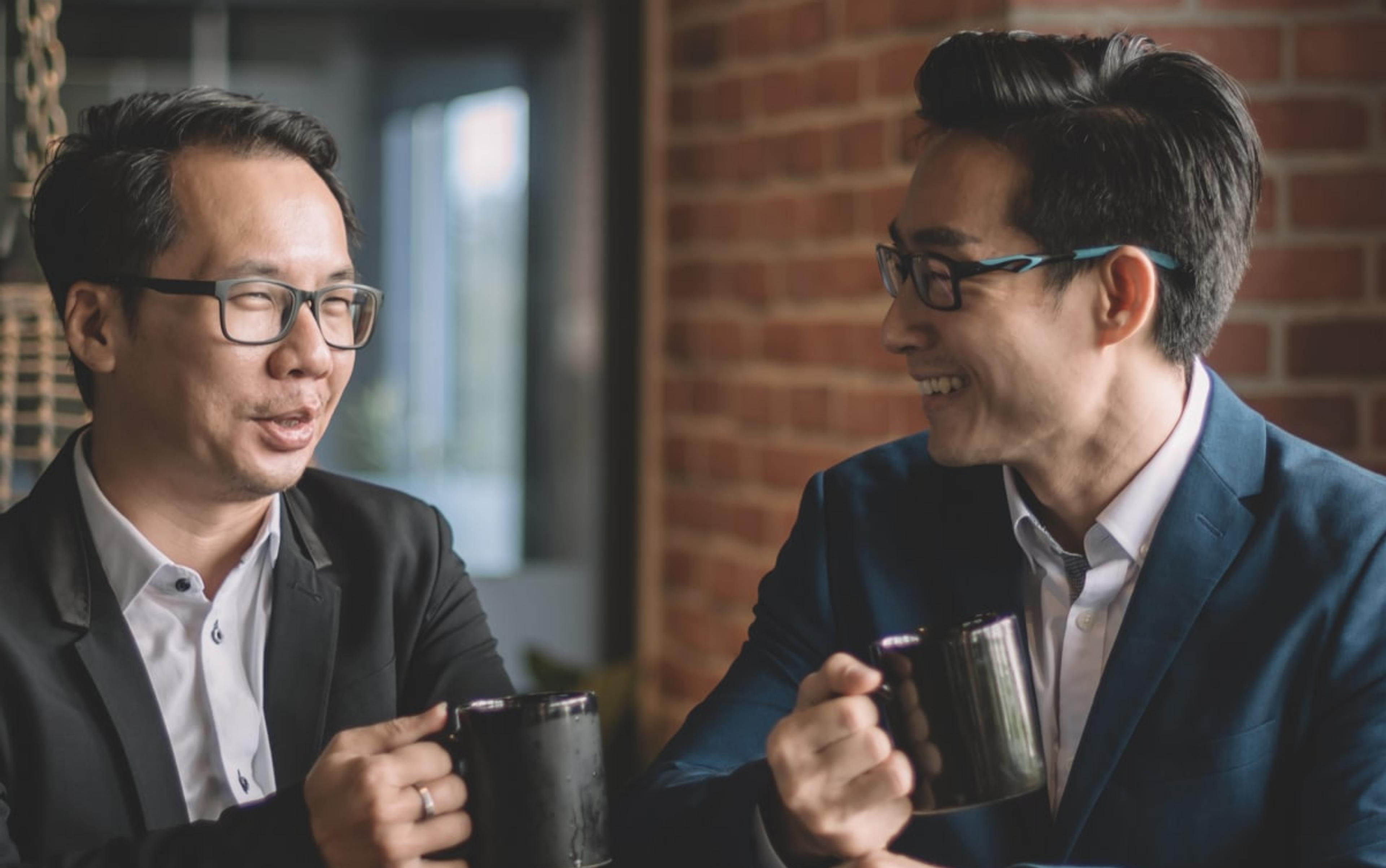 Two business professionals enjoying a casual conversation over coffee, illustrating the supportive environment of Adapt's coaching services.