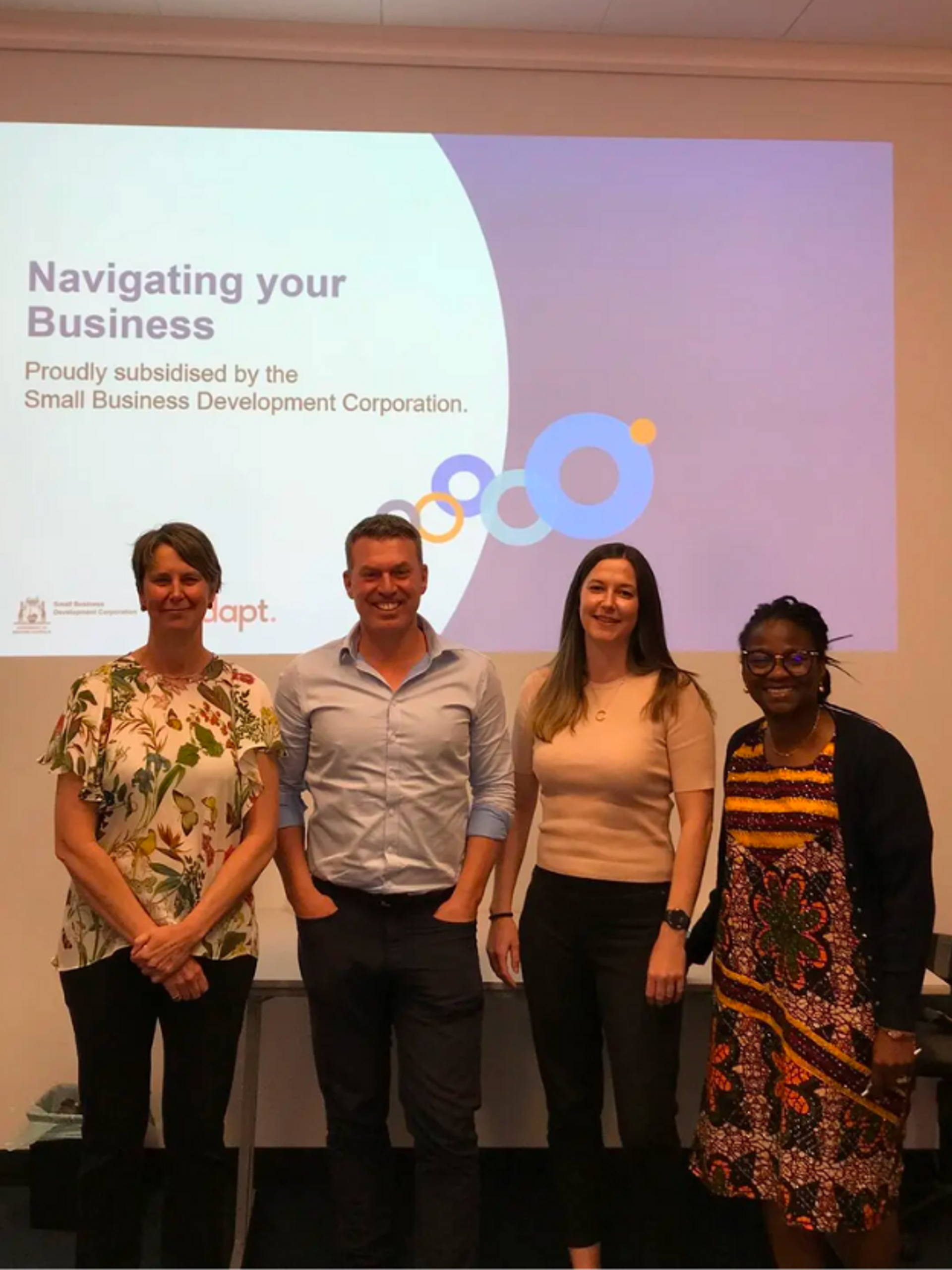 Group photo of business workshop participants with a 'Navigating your Business' presentation slide in the background.
