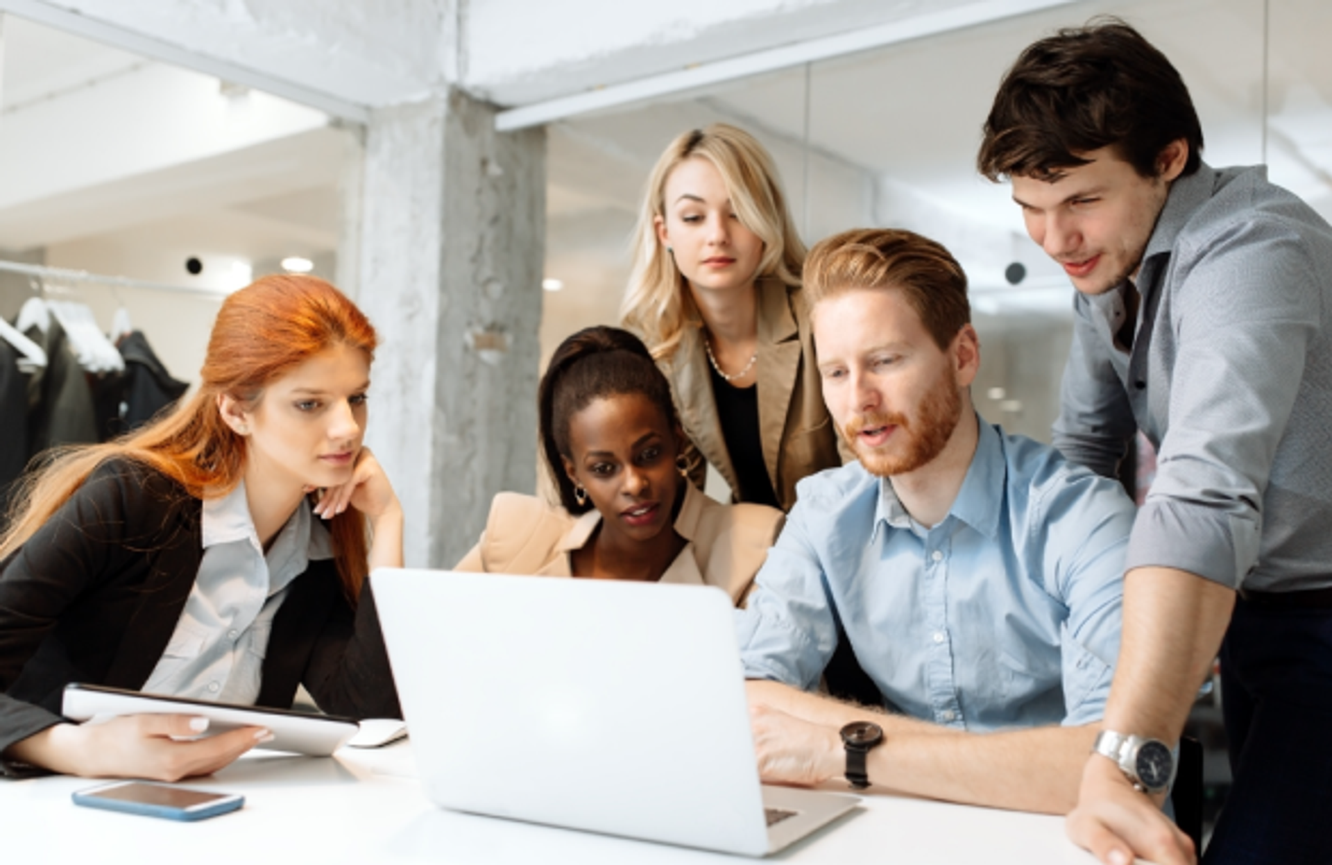 A diverse group of business professionals gathered around a laptop, engaged in a collaborative discussion, representing the strategic planning and teamwork of the Adapt leadership team.