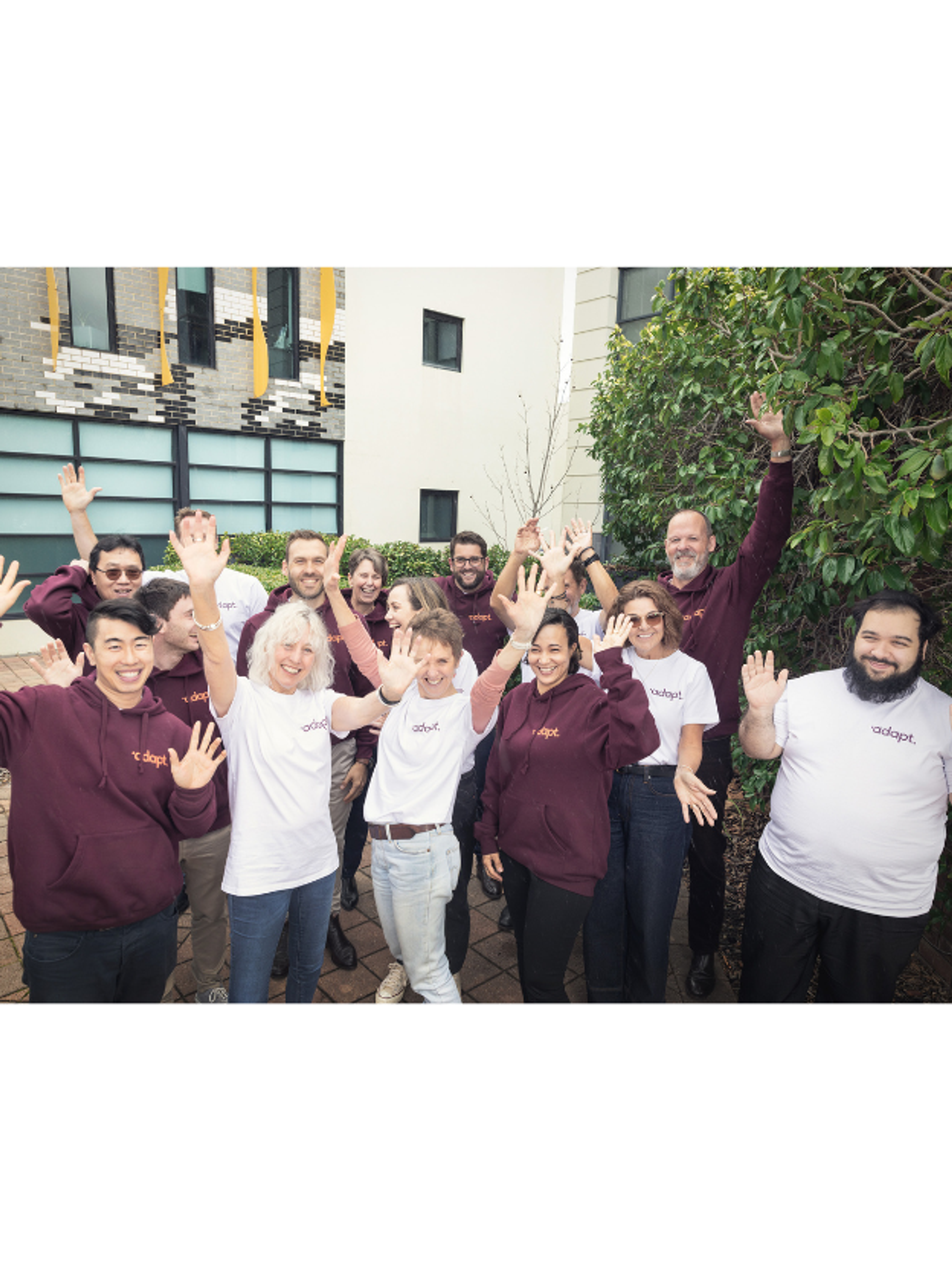 Adapt team members celebrating outdoors, wearing Adapt hoodies and T-shirts, with hands raised in excitement.