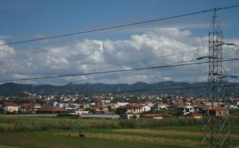 Xhafzotaj seen across the fields, with the hills behind, Albania — Aktron (Wikimedia Commons)