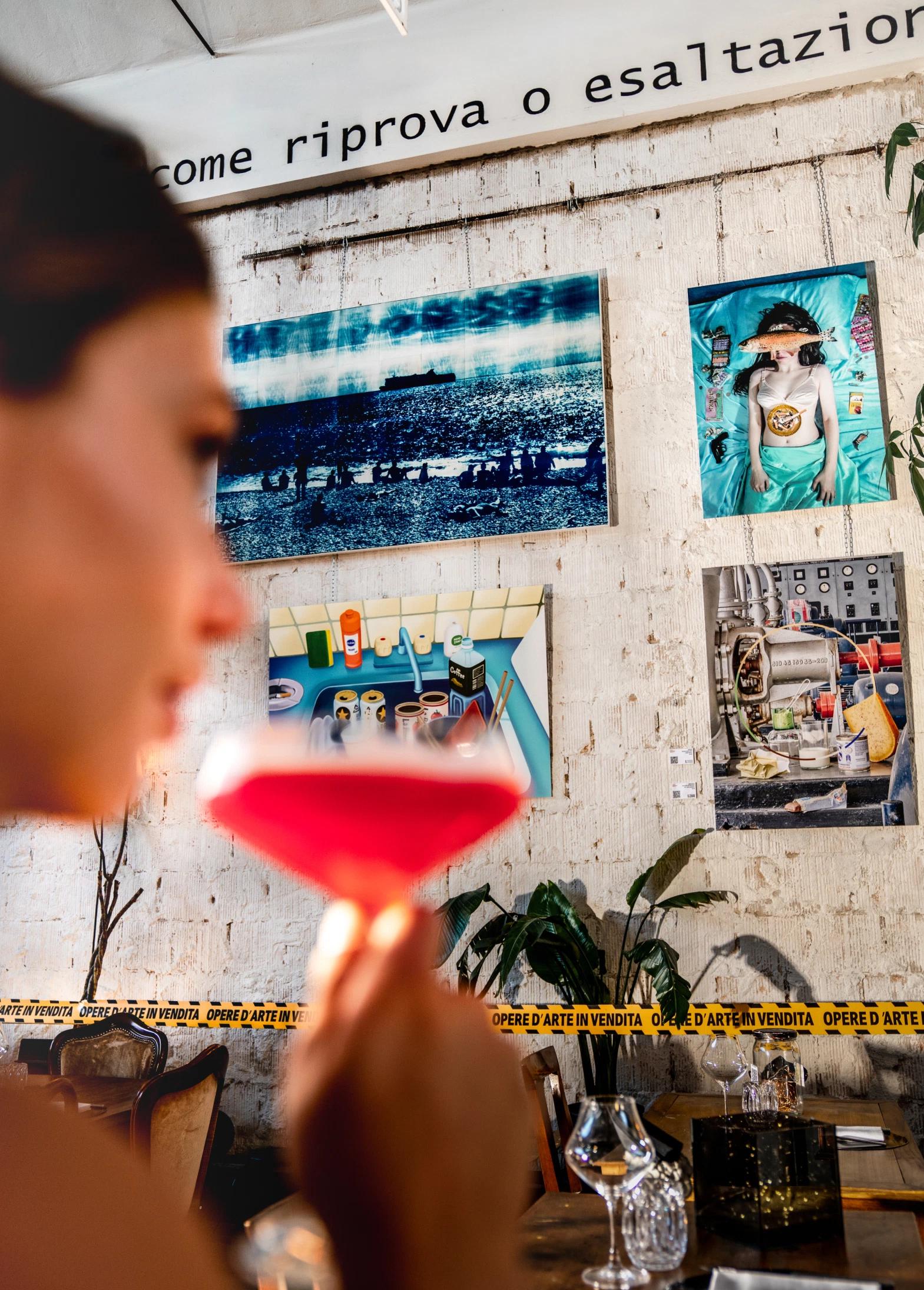 Una ragazza che sorseggia un drink davanti a dei quadri ne Il Cantiere Treviso