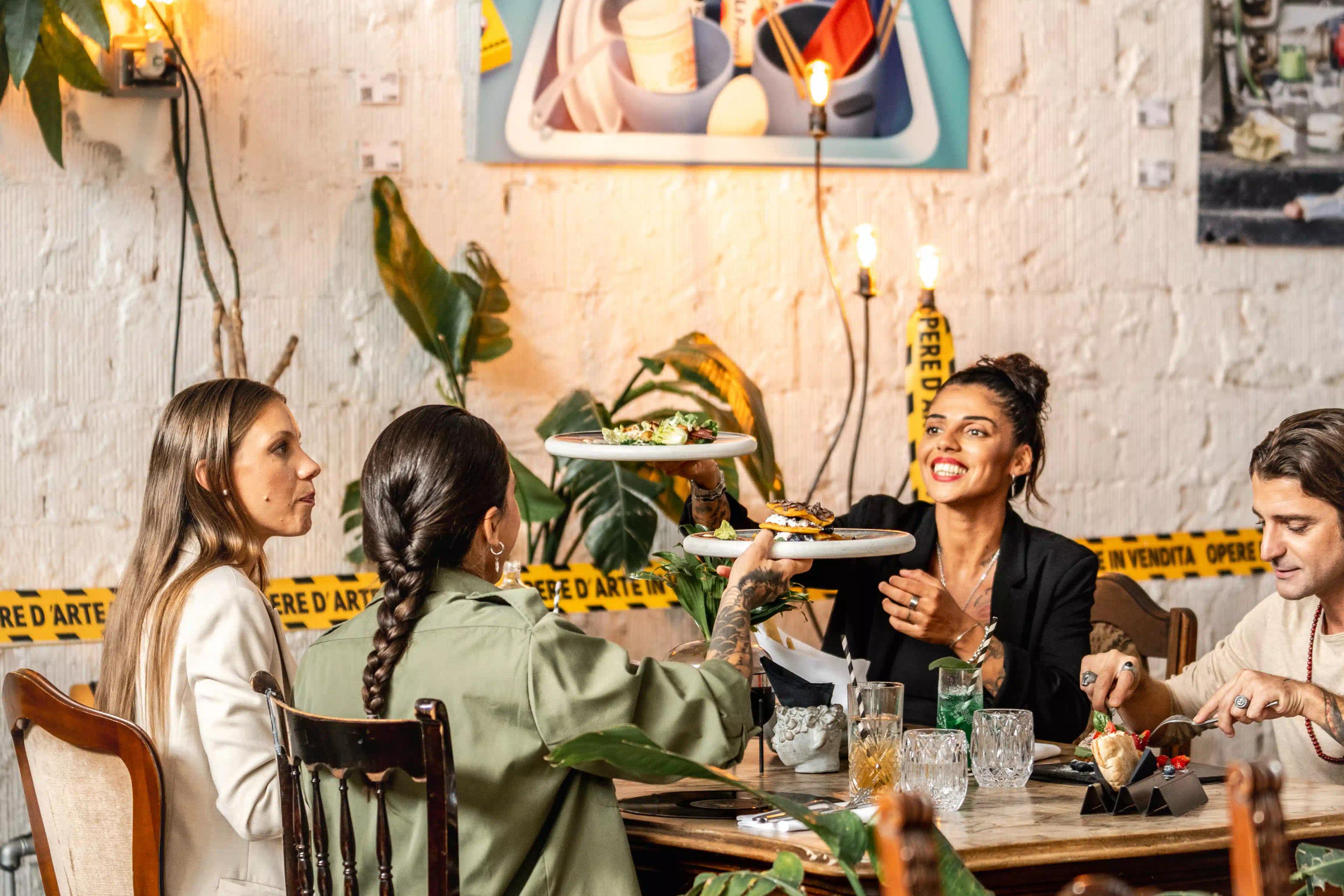 Un gruppo di persone sedute attorno ad un tavolo che ridono e mangiano