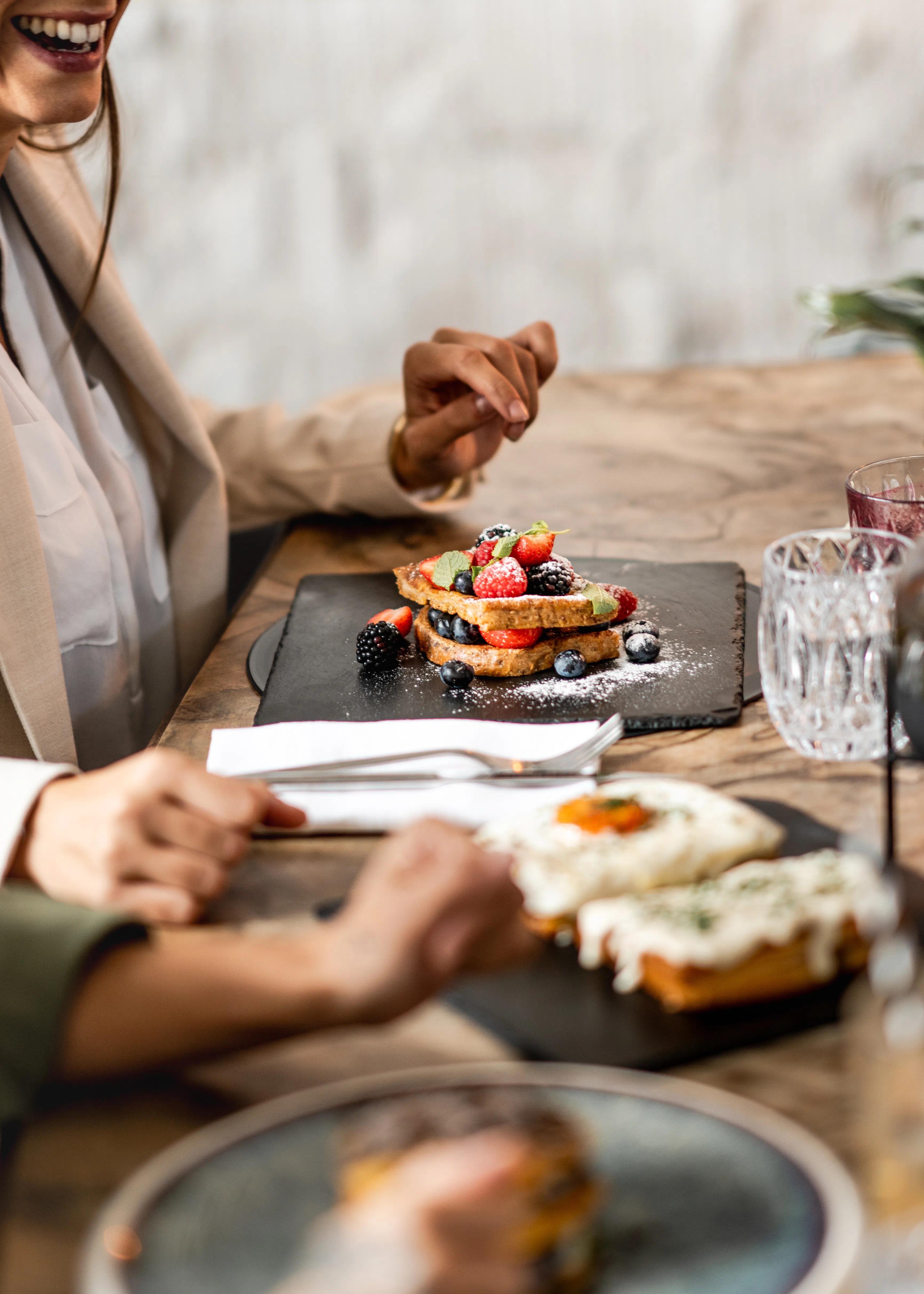 Una ragazza che ride davanti a dei pancakes con i frutti di bosco