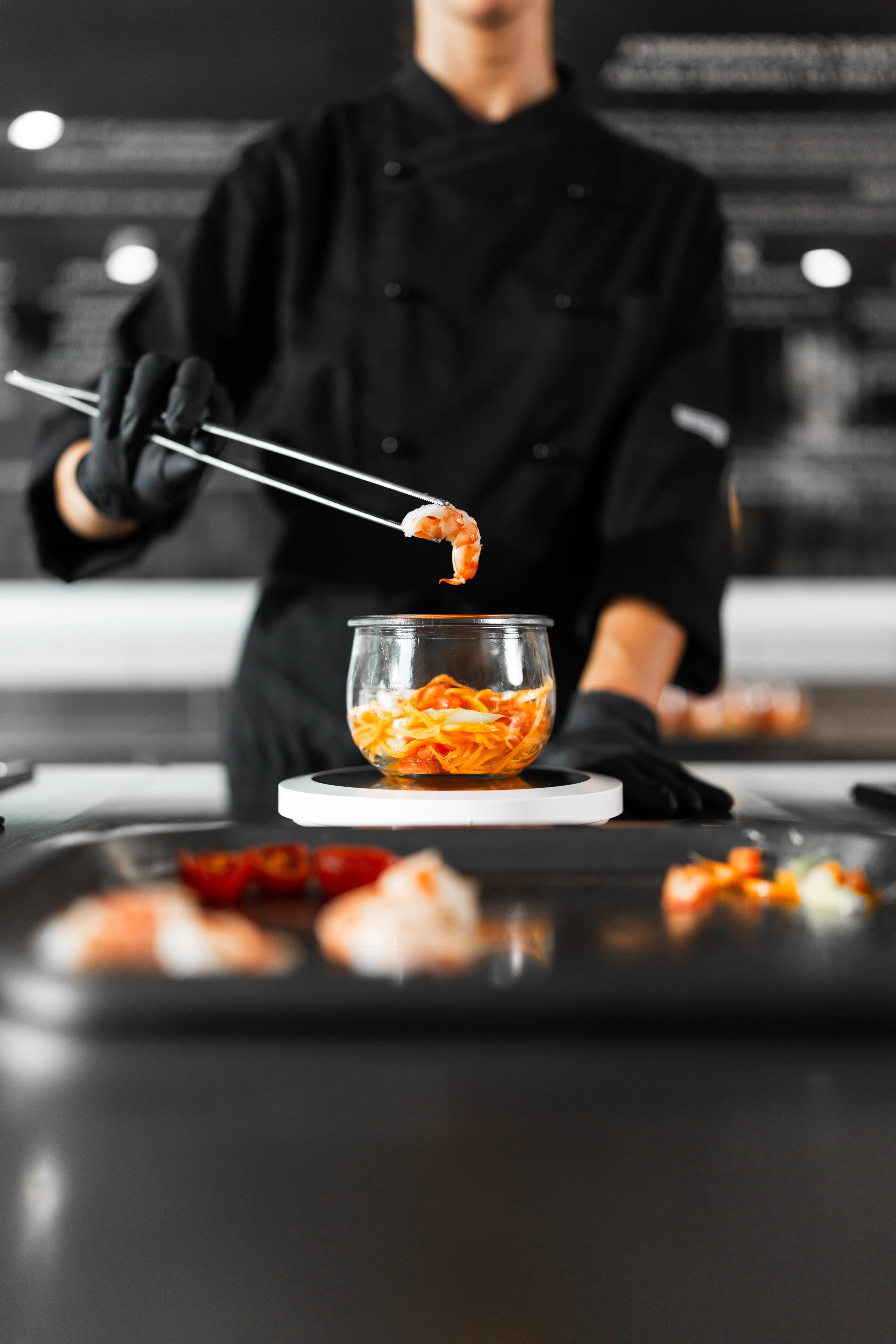 Chef che sta componendo un vaso Vite con un gamberetto tra le pinze