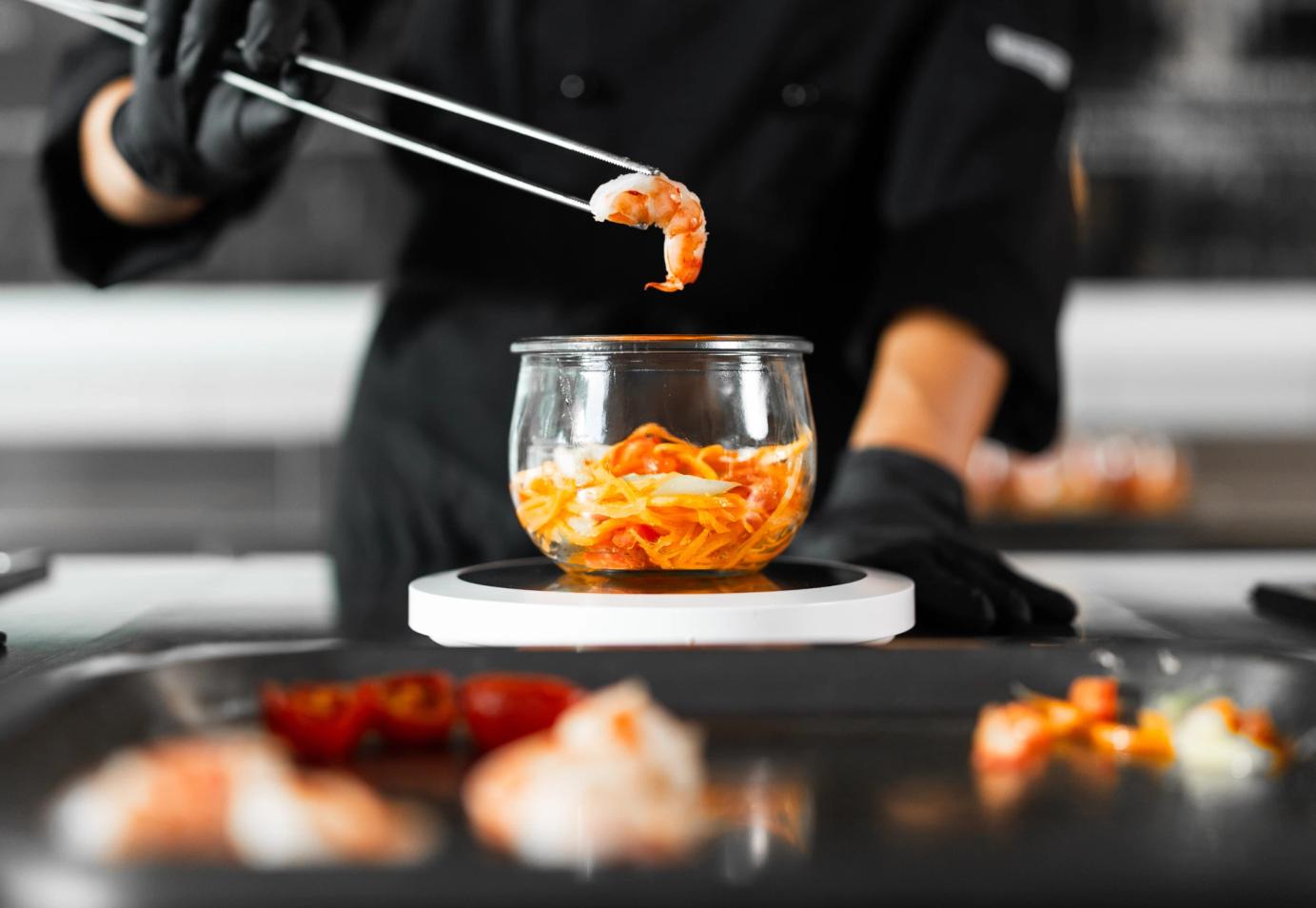 Chef che sta componendo un vaso Vite con un gamberetto tra le pinze