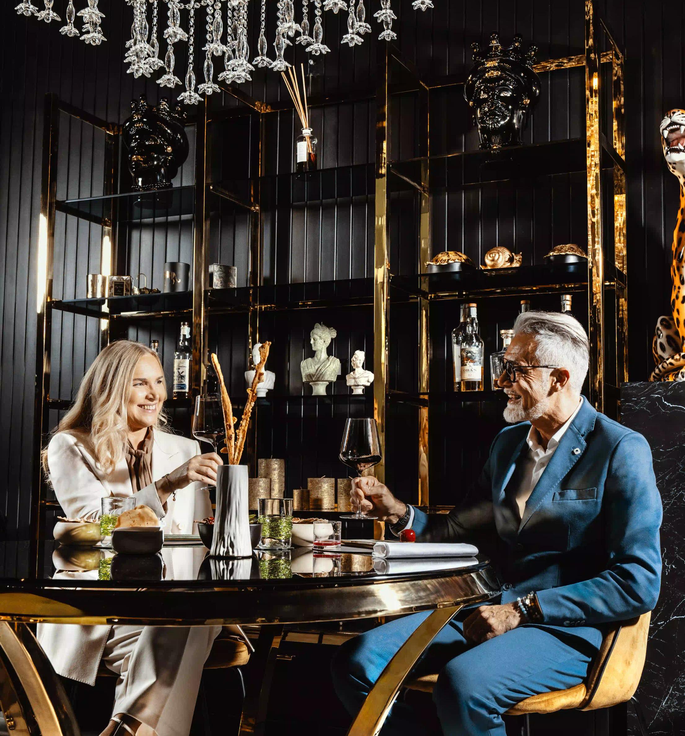 Un uomo e una donna seduti attorno ad un tavolo di Vite Restaurant Treviso che brindano mentre sorridono