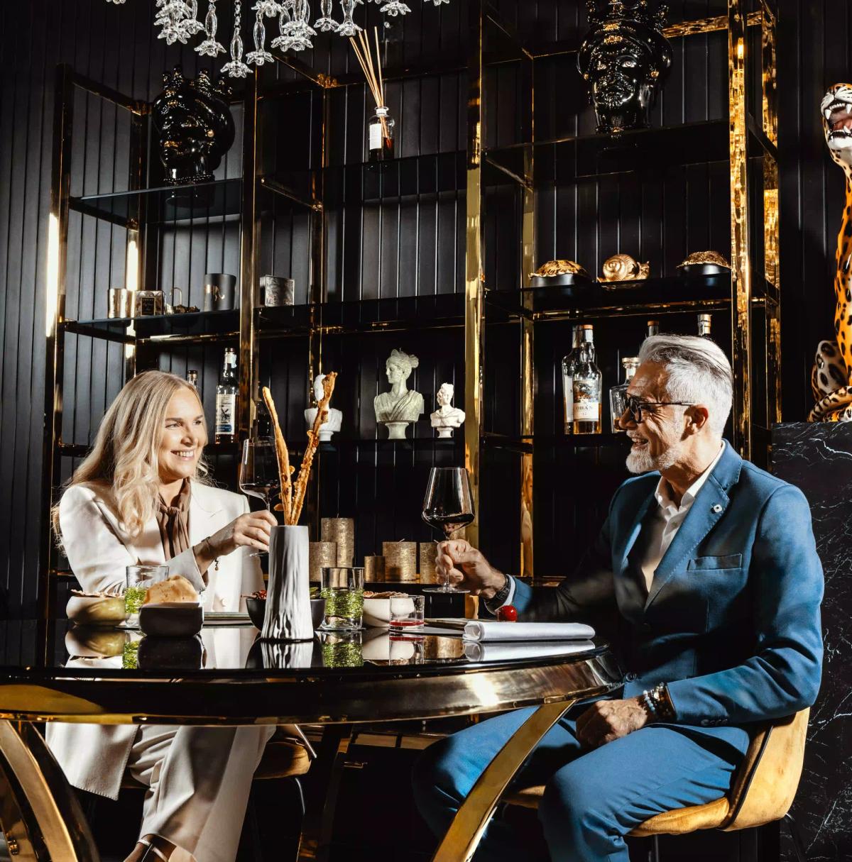 Un uomo e una donna seduti attorno ad un tavolo di Vite Restaurant Treviso che brindano mentre sorridono