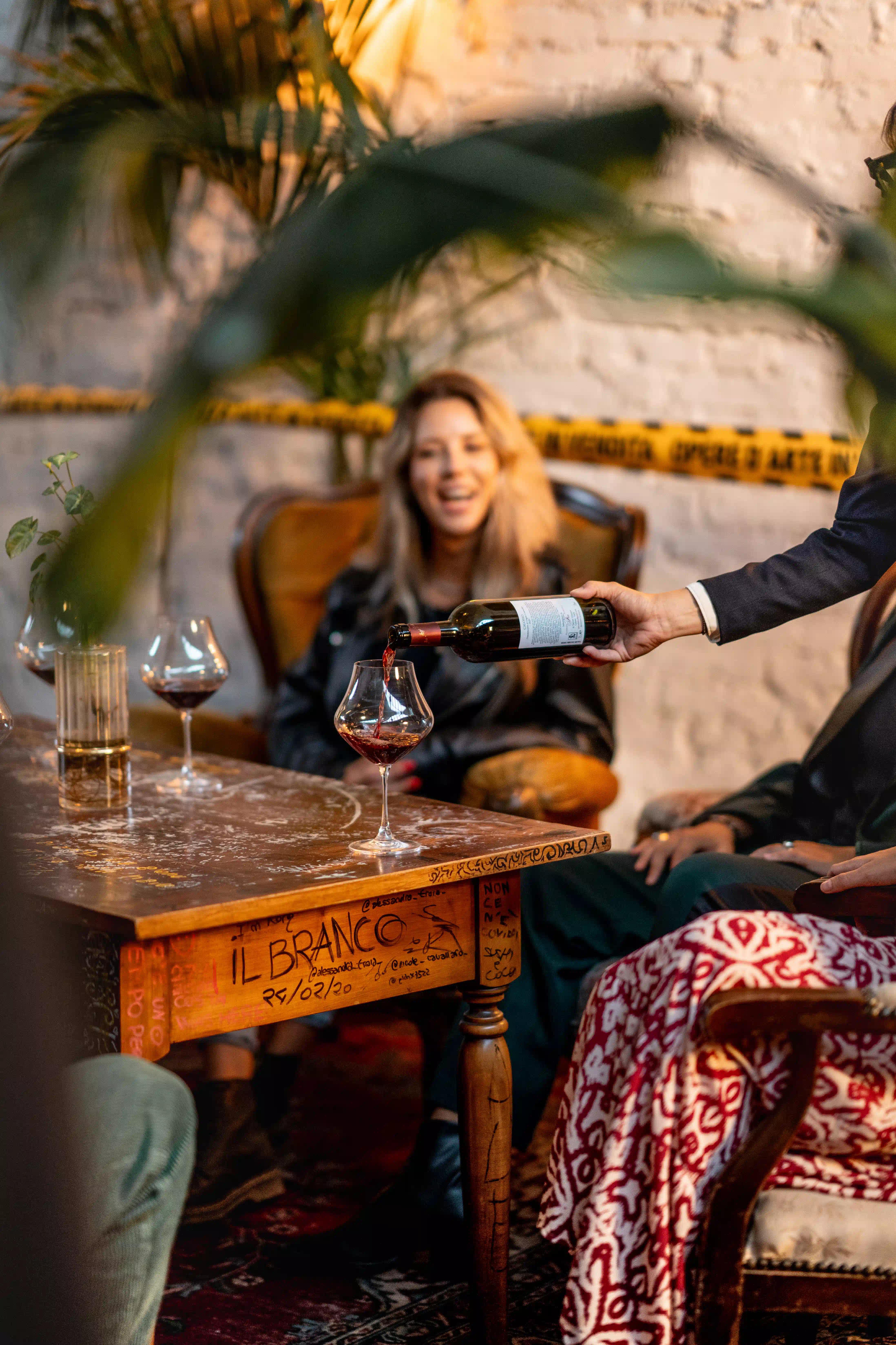 Sommelier che serve vino rosso ad una ragazza seduta attorno al tavolo