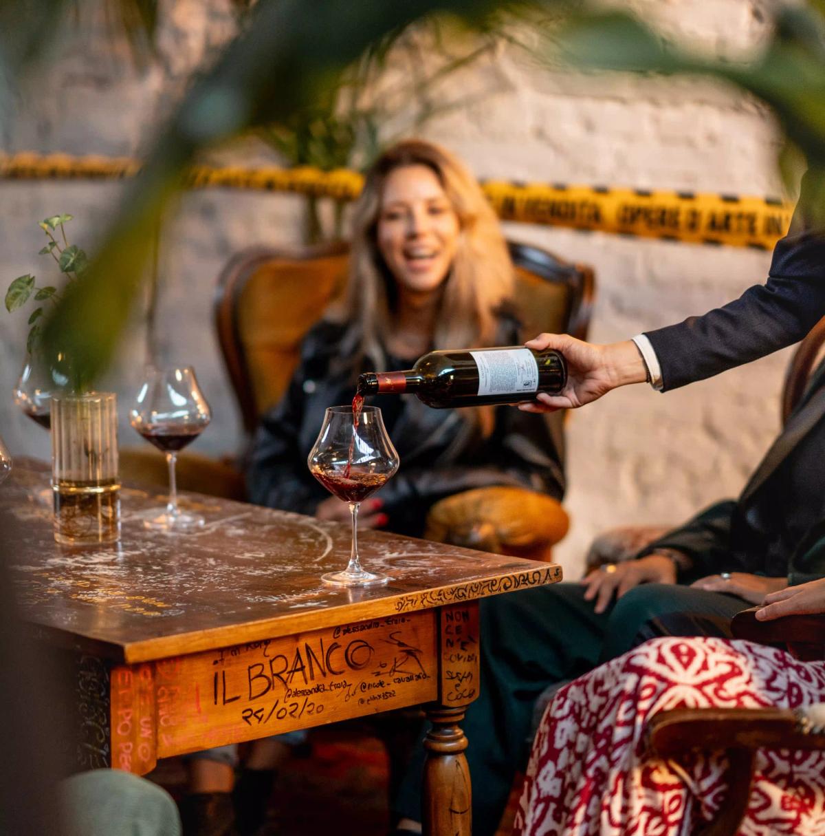 Sommelier che serve vino rosso ad una ragazza seduta attorno al tavolo