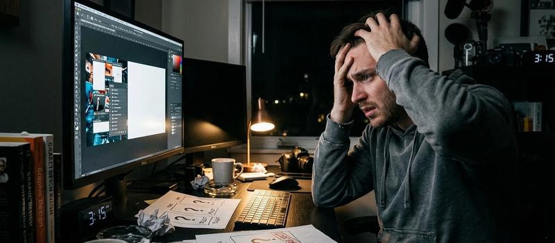 An European-American creator is sitting at the computer desk, looking extremely anxious and troubled, struggling with the design of the video cover. The overall environment is dim, indicating that the creator is working late into the night and putting in extra effort to create