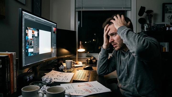 An European-American creator is sitting at the computer desk, looking extremely anxious and troubled, struggling with the design of the video cover. The overall environment is dim, indicating that the creator is working late into the night and putting in extra effort to create