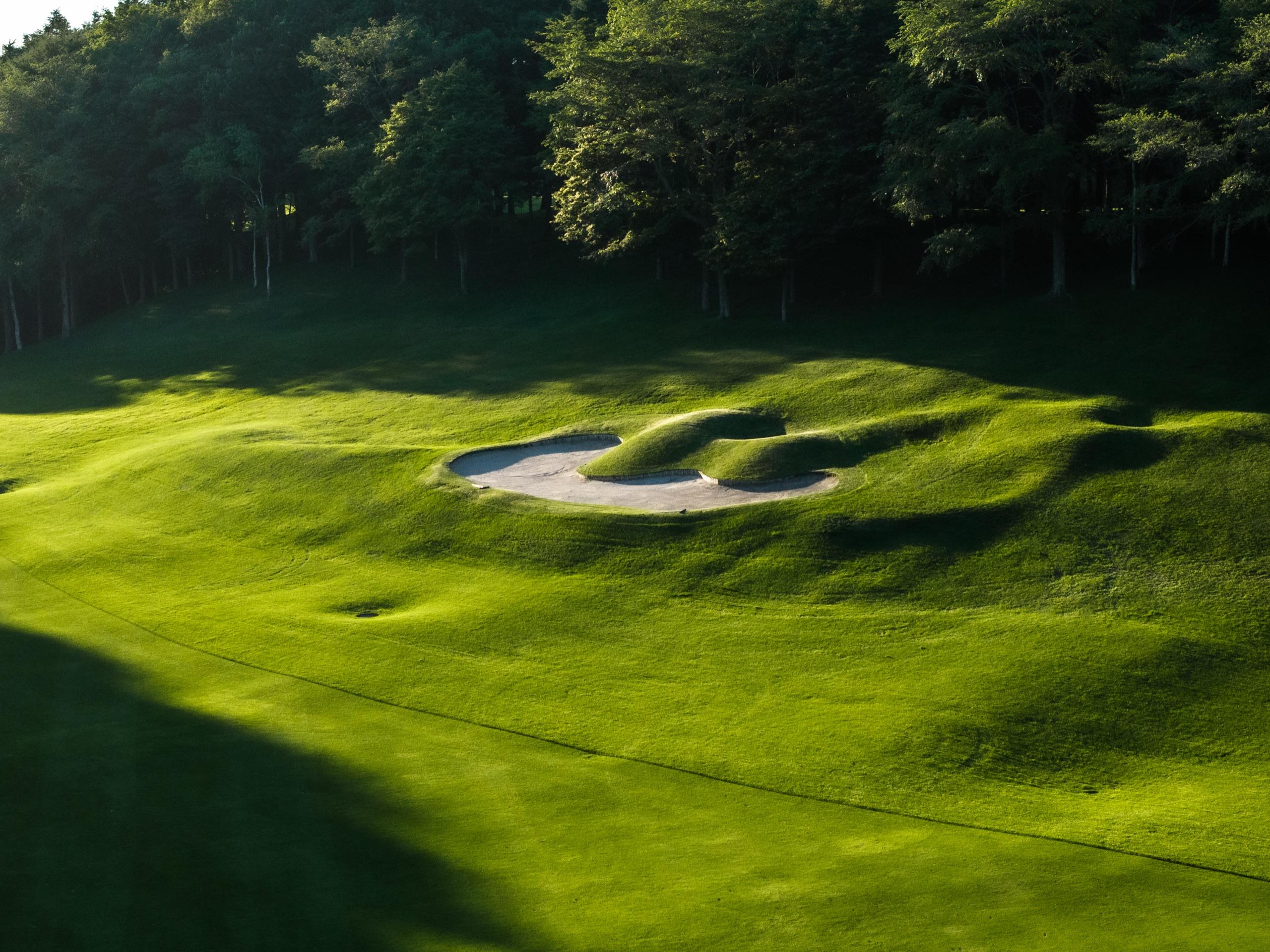 Sculpted cluster bunker cut into rolling mounds of rough in low evening light