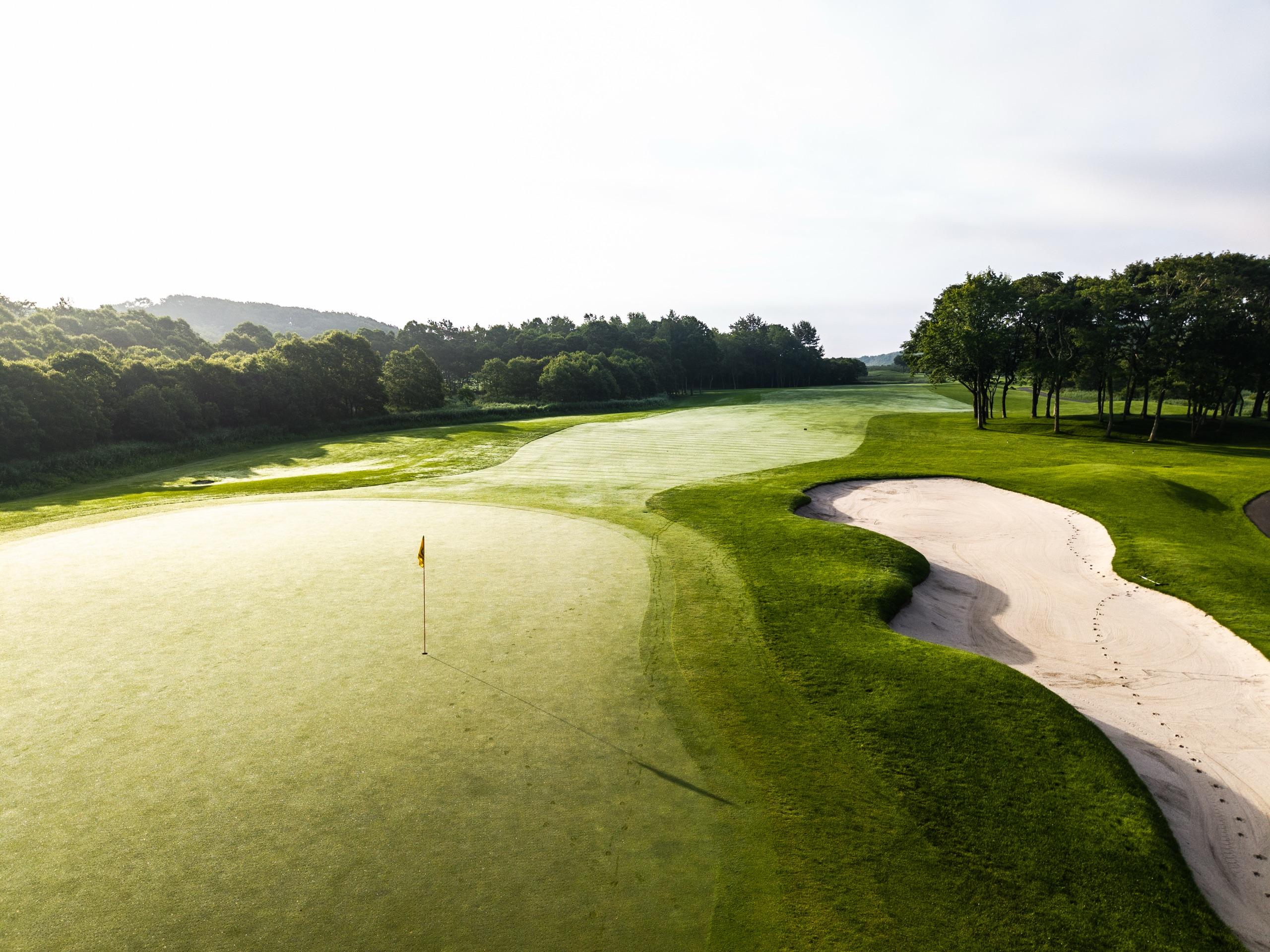 Dew-covered green and yellow flag beside a long sprawling bunker in early morning light