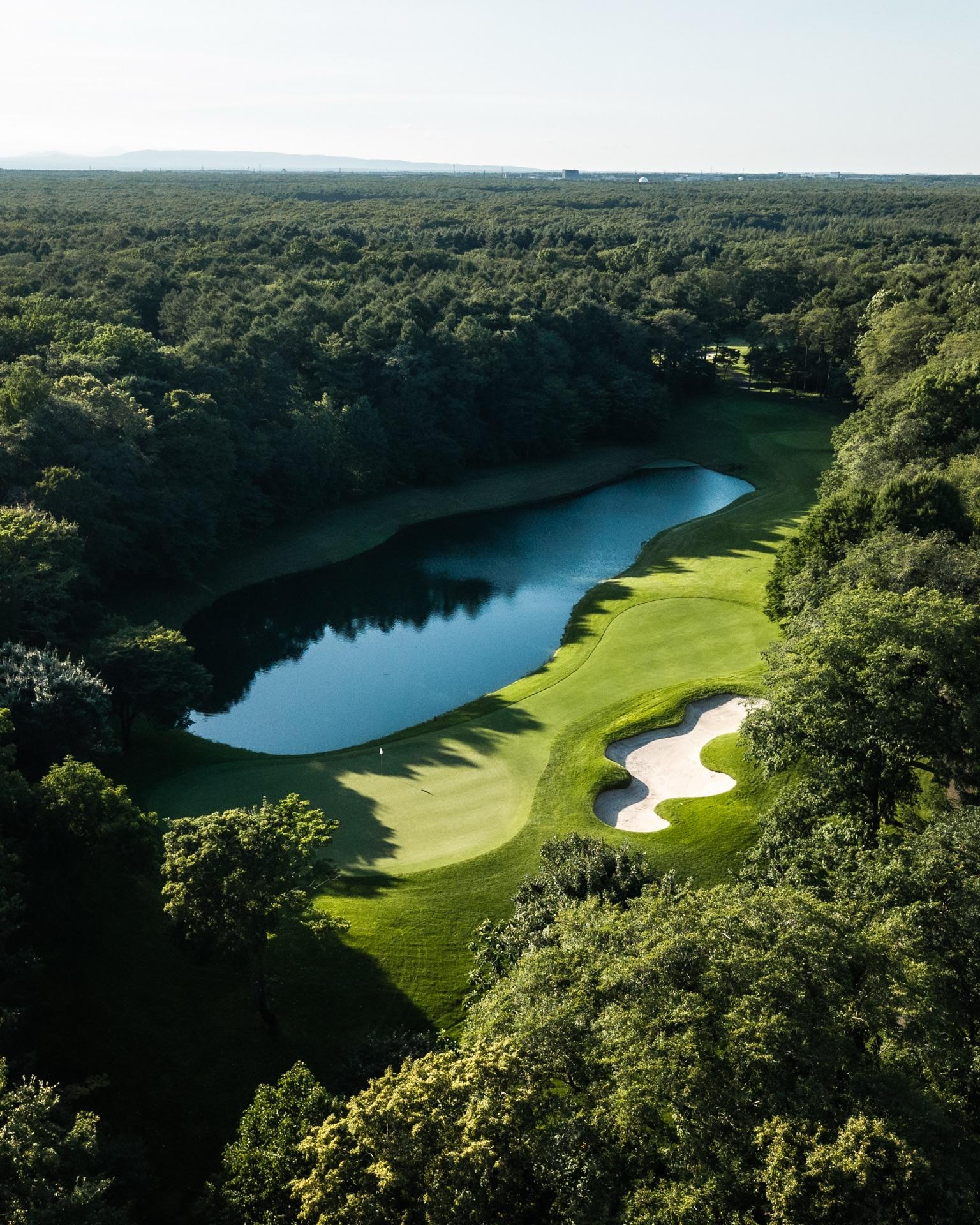 Aerial view of a green and white bunkers beside a lake, surrounded by unbroken Hokkaido forest