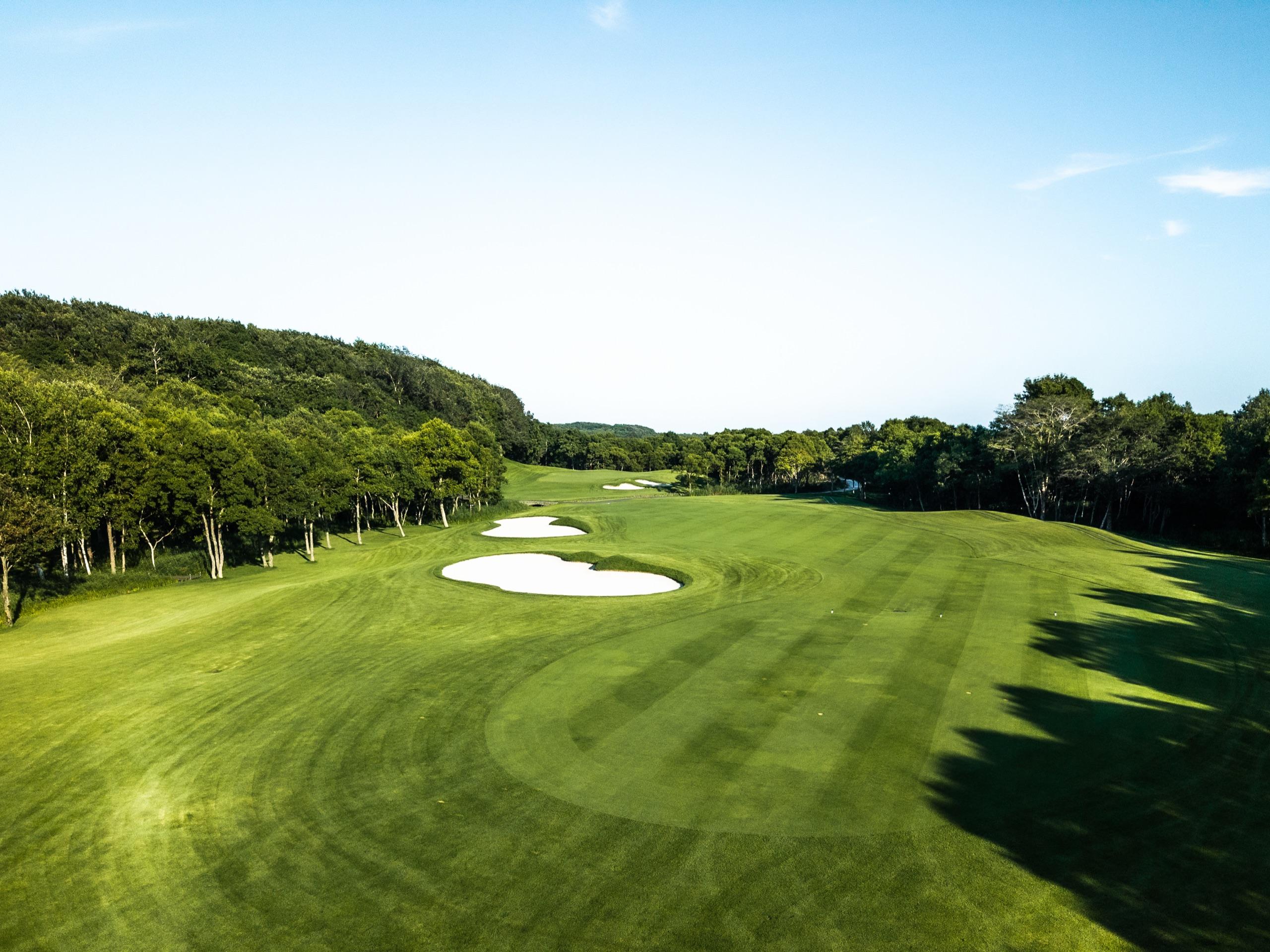 Tree-lined fairway with twin fairway bunkers under a clear blue Hokkaido sky