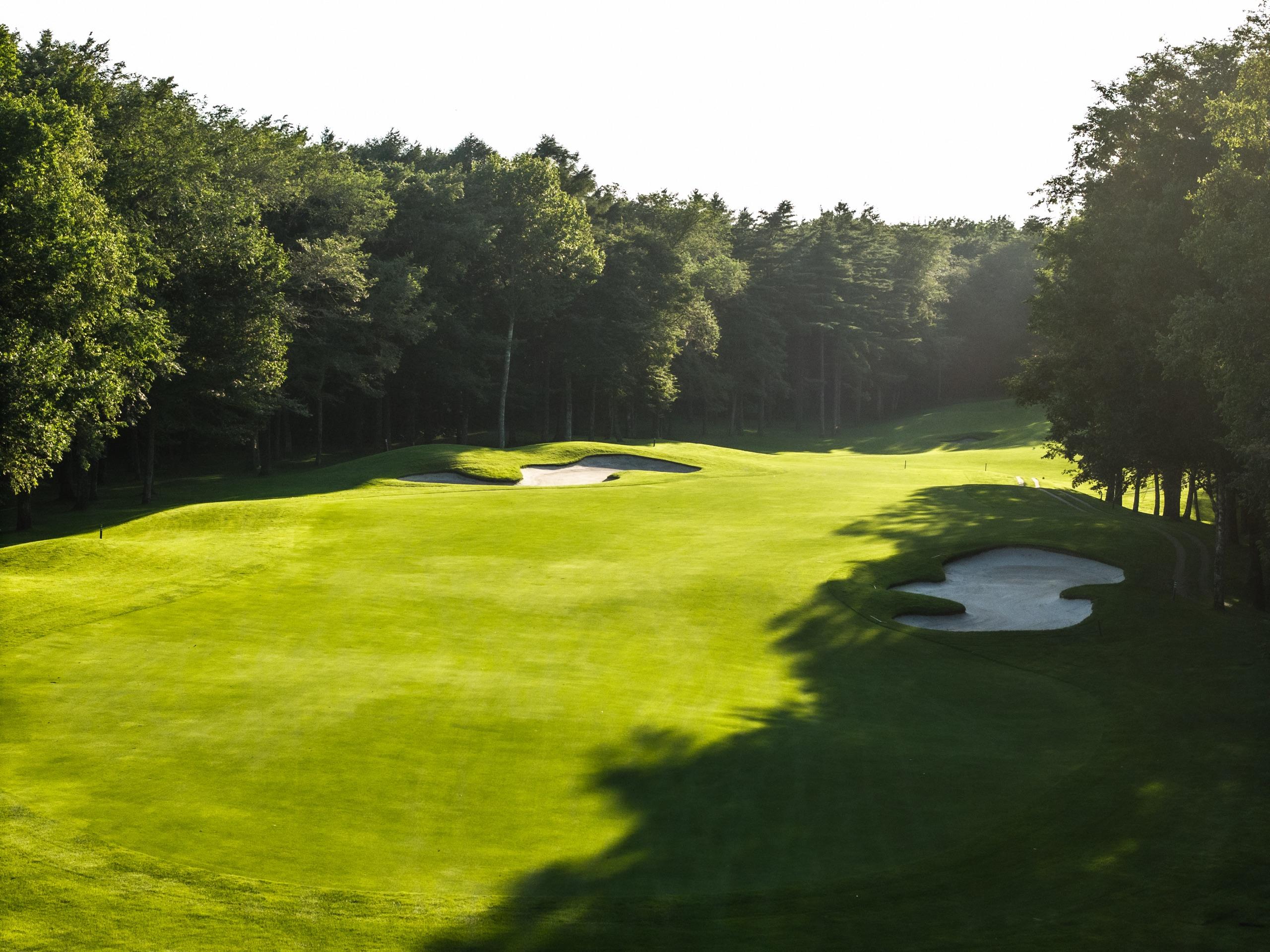 Broad fairway flanked by clusters of white sand bunkers in evening light