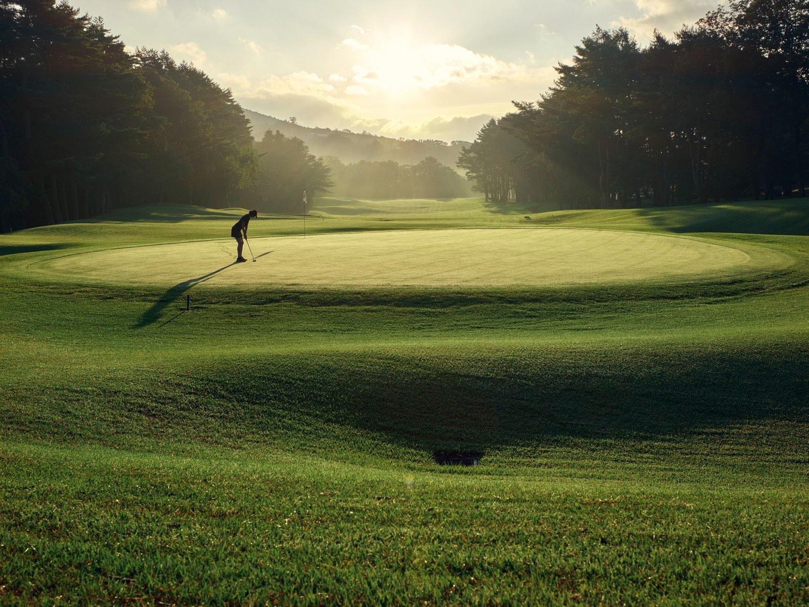 Golfer putting on a Kagosaka Course green at golden hour