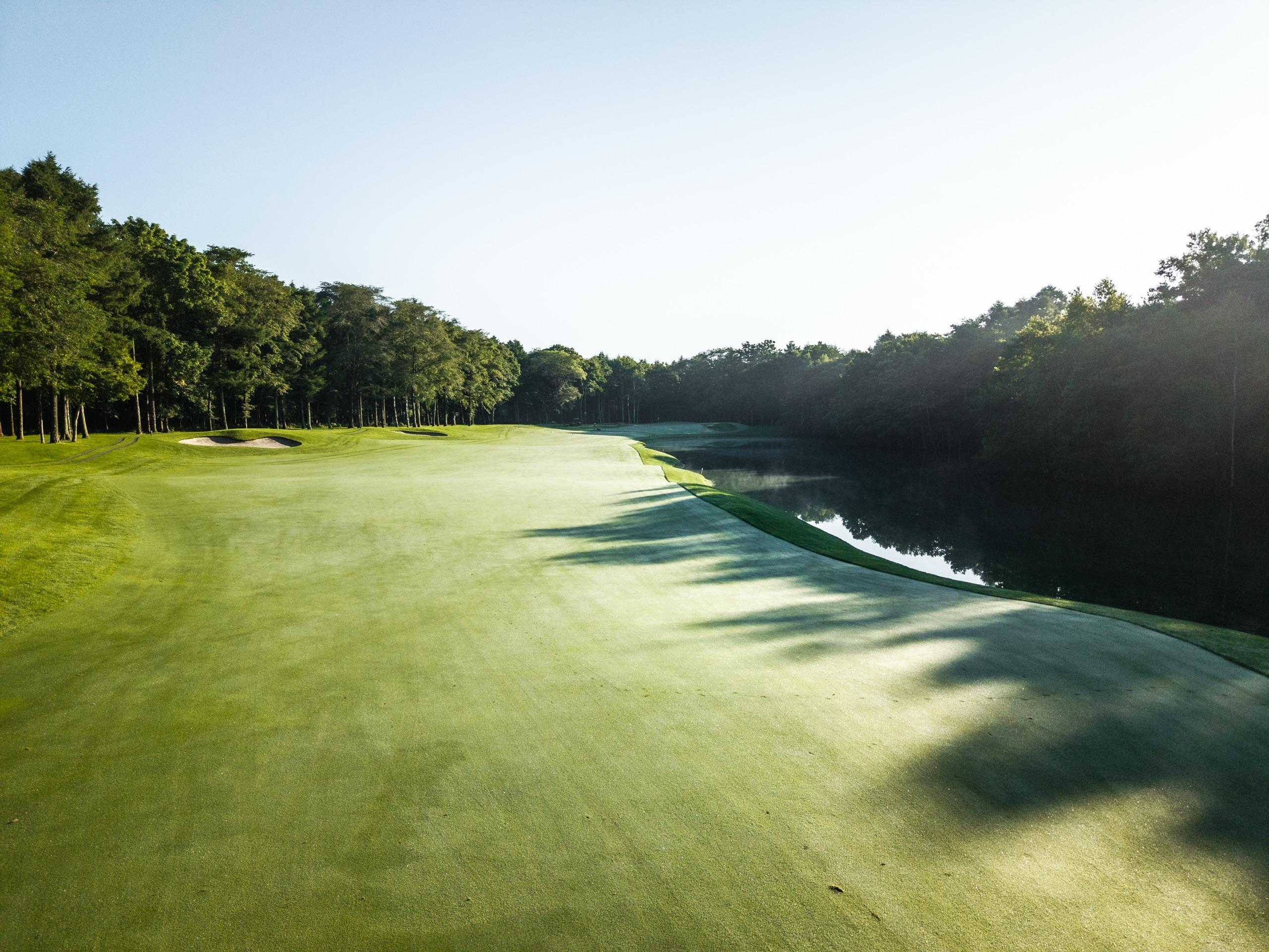 Broad fairway sweeping past a lake half in morning shadow