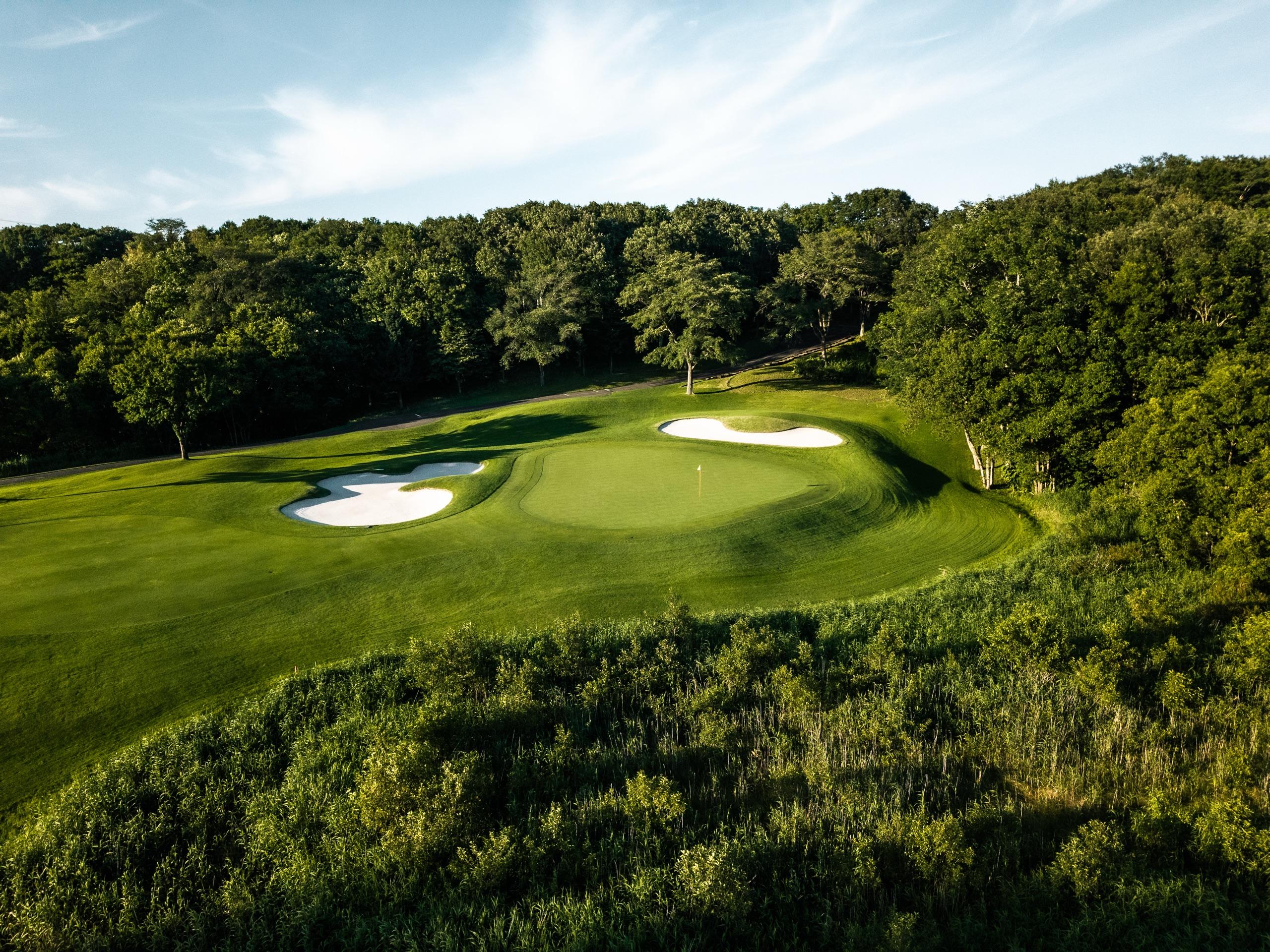 Elevated green with two white bunkers carved out of thick forest in golden evening light