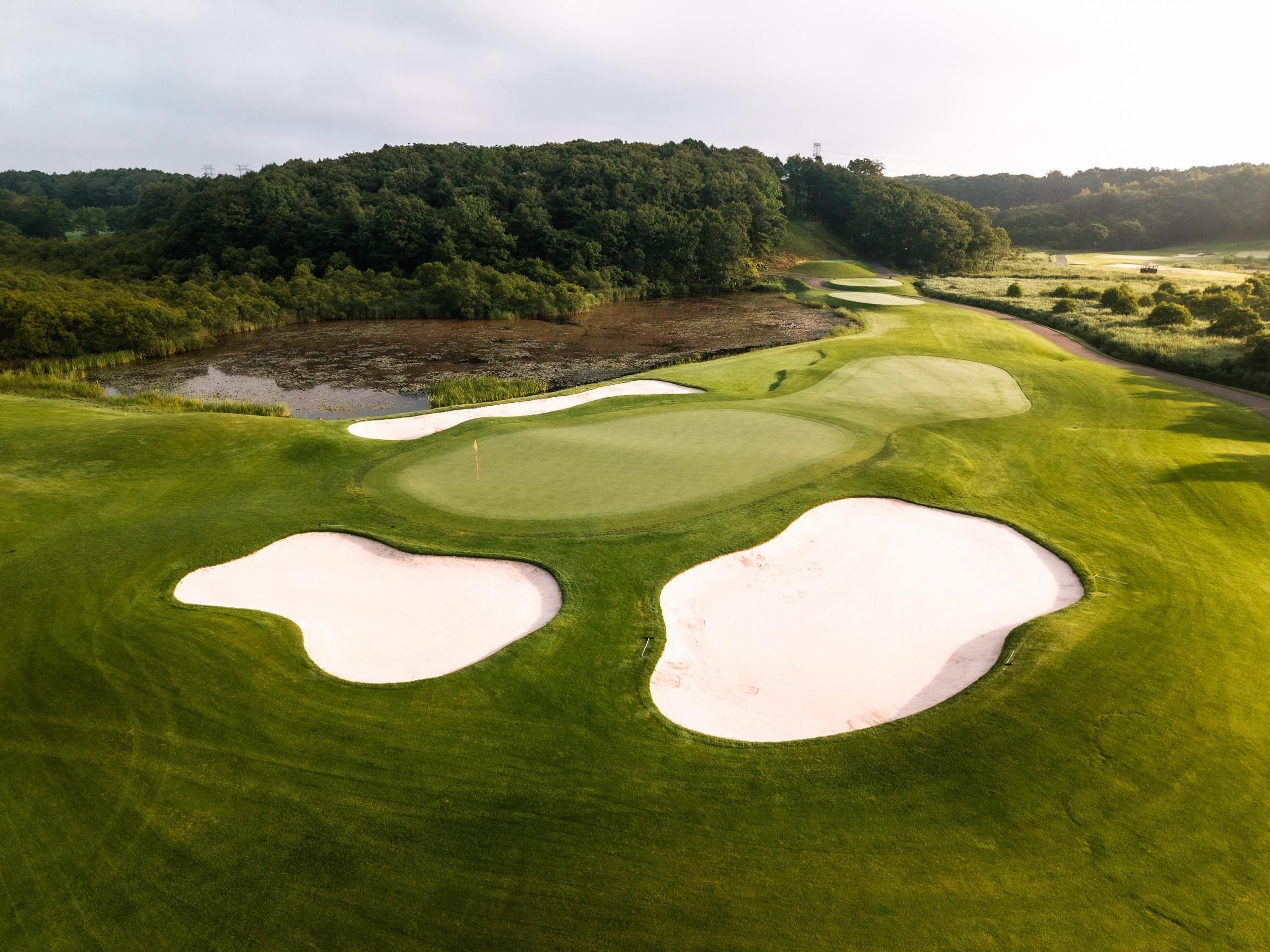 Green complex guarded by three white sand bunkers, with a marsh pond and dense forest behind at Hokkaido Brooks Country Club