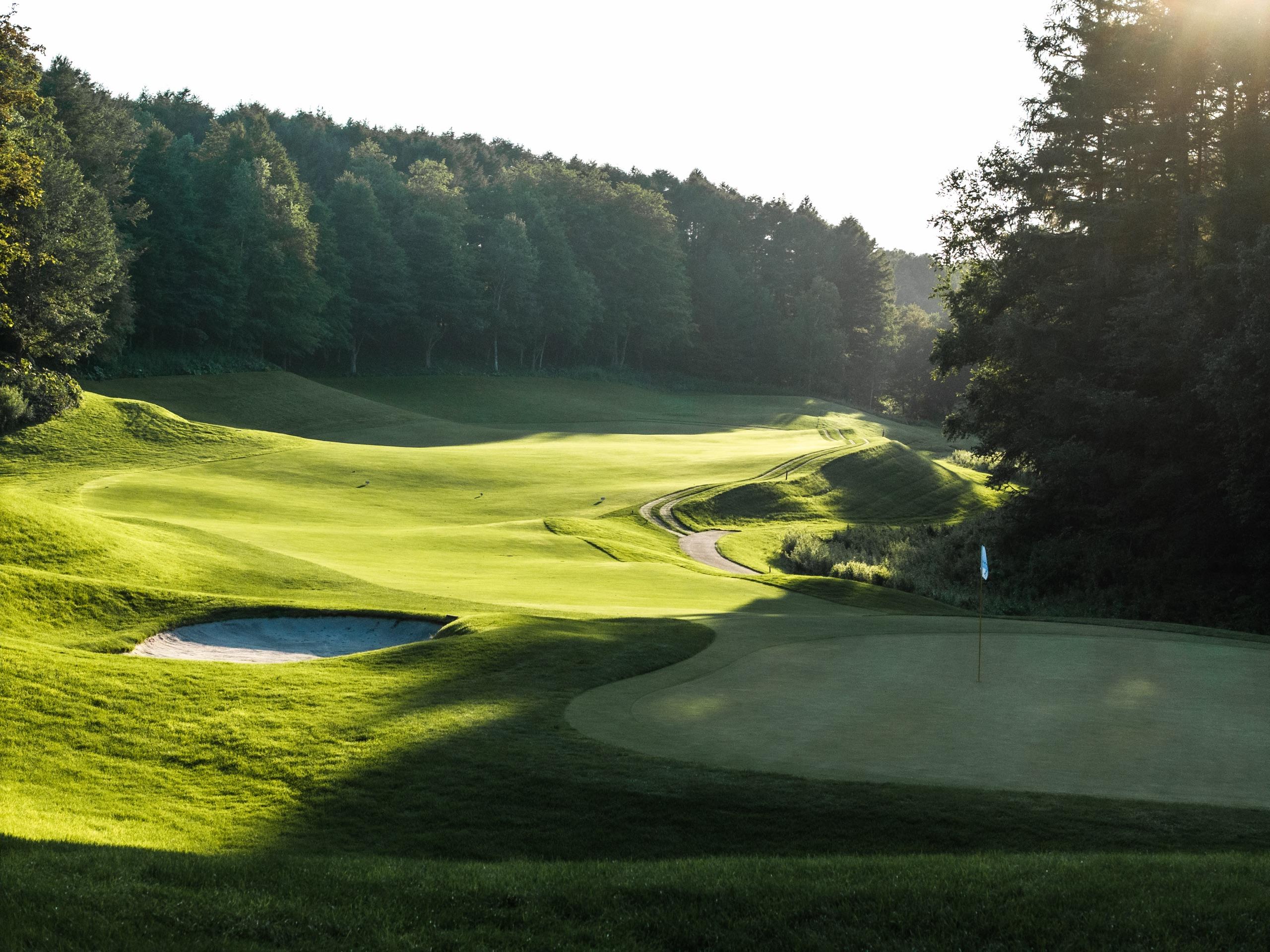 Evening light across rolling fairways with a greenside bunker in the foreground