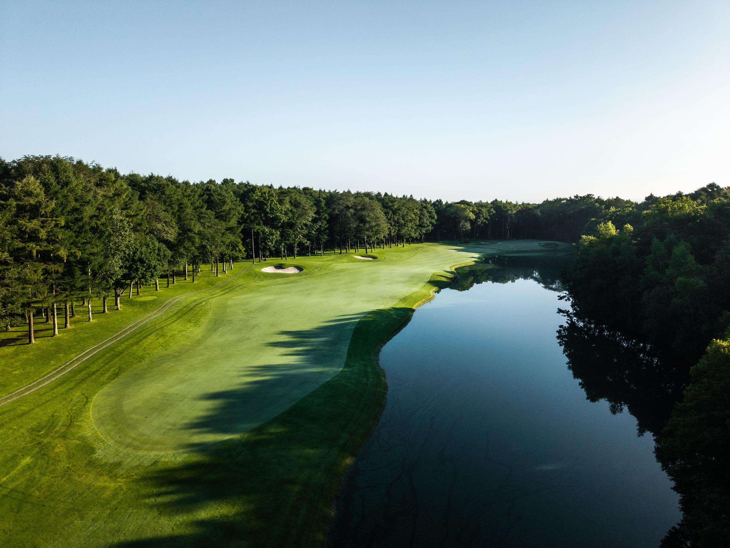 Fairway curving along the edge of a still pond bordered by pine forest
