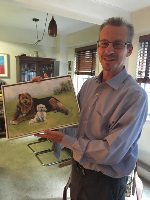 Dan holding the painting of two dogs, Hero and Leah, lying on the grass.