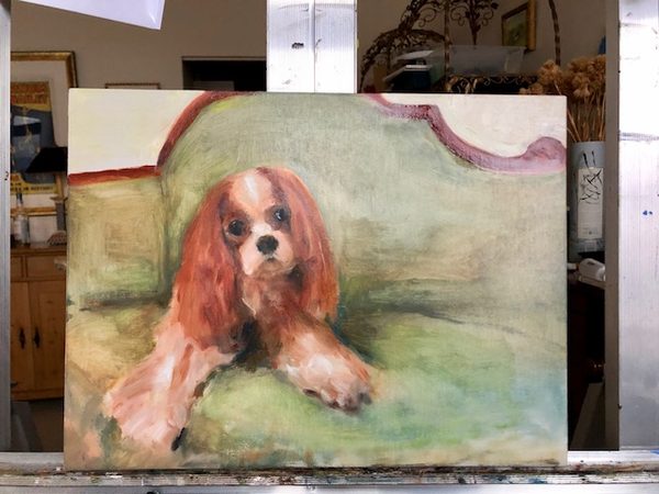 The painting of Lily, a King Charles spaniel on a green sofa, on an easel.