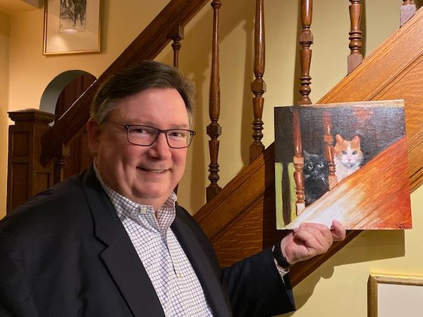 Michael Yon holding up the painting of two cats on a staircase.
