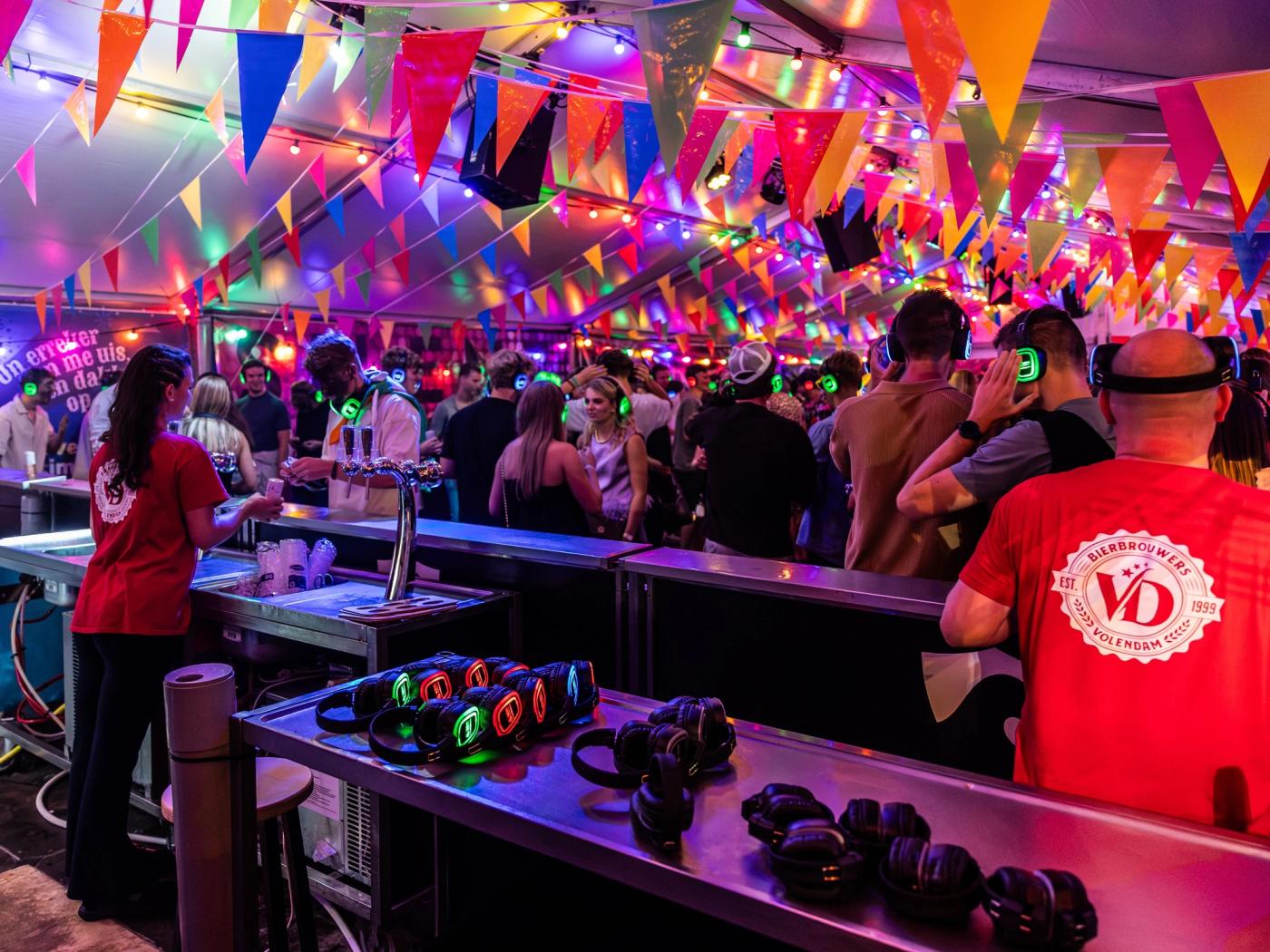 Volle feesttent met gasten die verlichte silent disco koptelefoons dragen