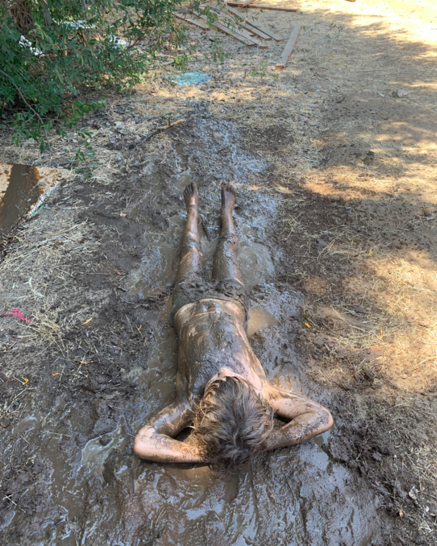 a child covered in mud lays in a mud stream