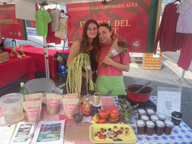 Two people at a farmers market booth, both holding flowers