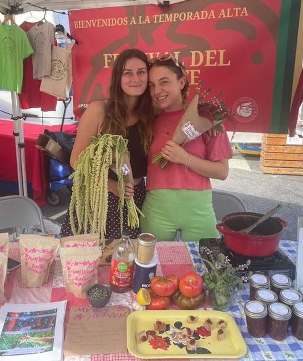 Two people at a farmers market booth, both holding flowers