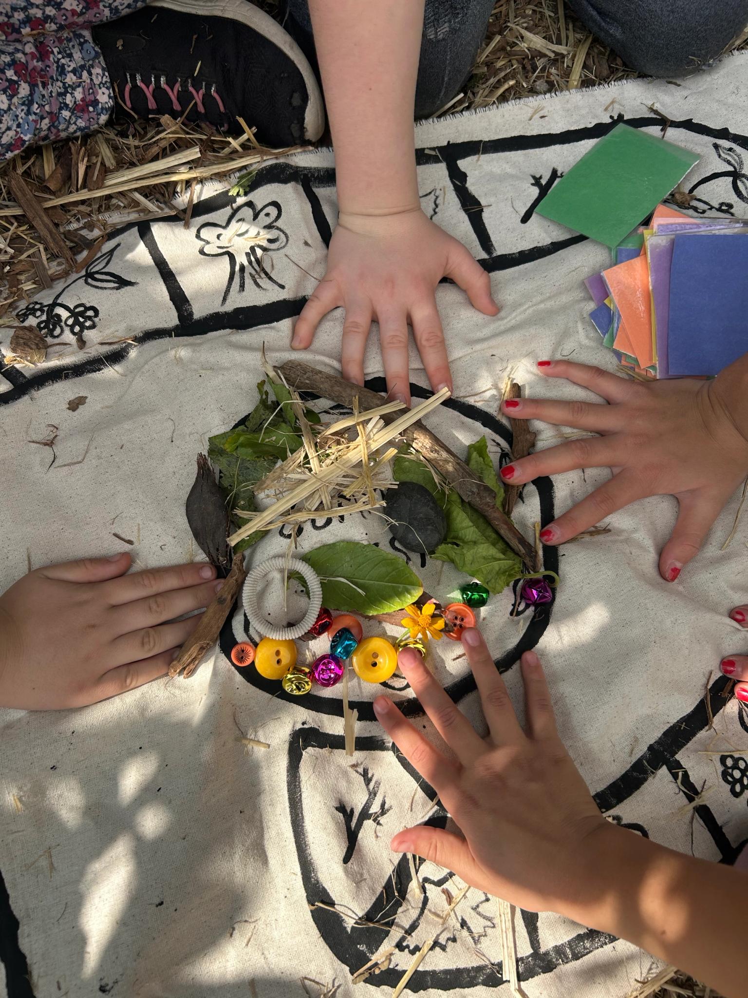4 kids hands surround the center of a board game about crows, the center is a community nest filled with treasures like twigs and shiny objects
