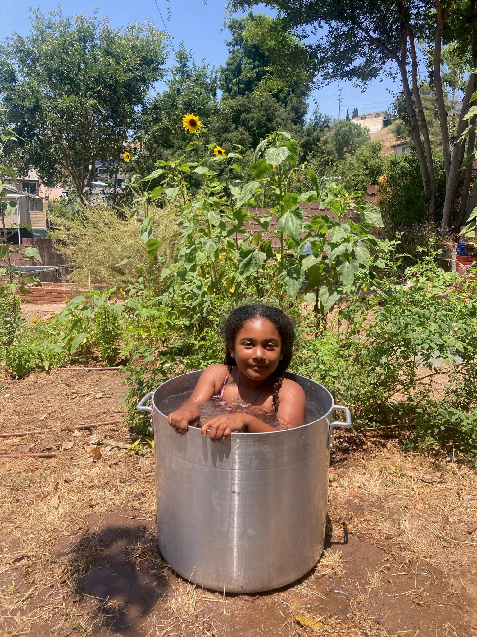 A child sits in a big stock pot full of water that we lovingly call the "farm jacuzzi"