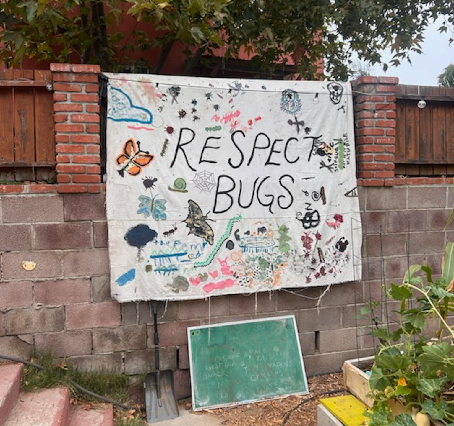a banner hangs from a wood and brick wall that reads "Respect Bugs" surrounded by children's art of bugs