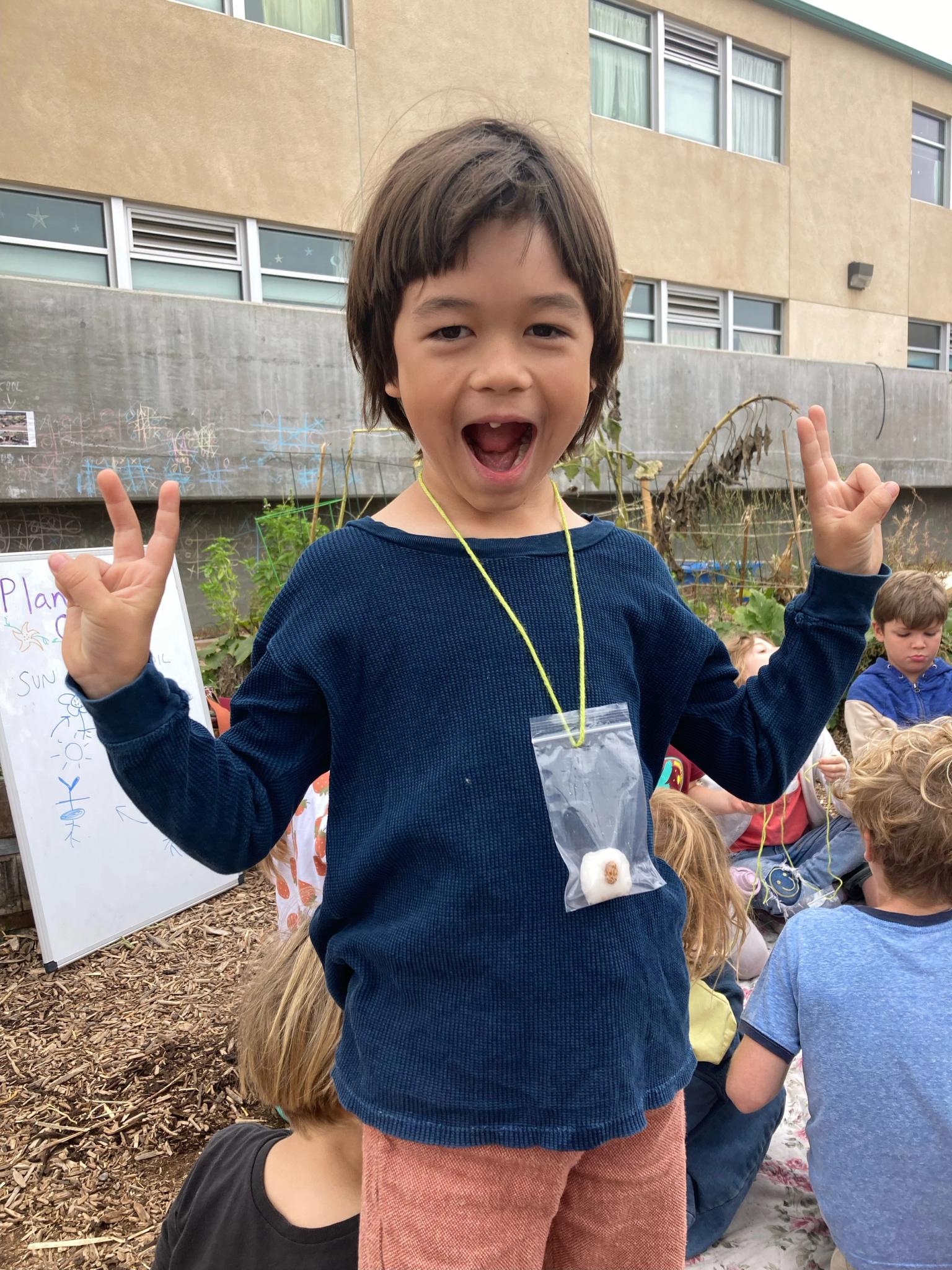 A child stands with peace signs and a "bean necklace" made during garden class