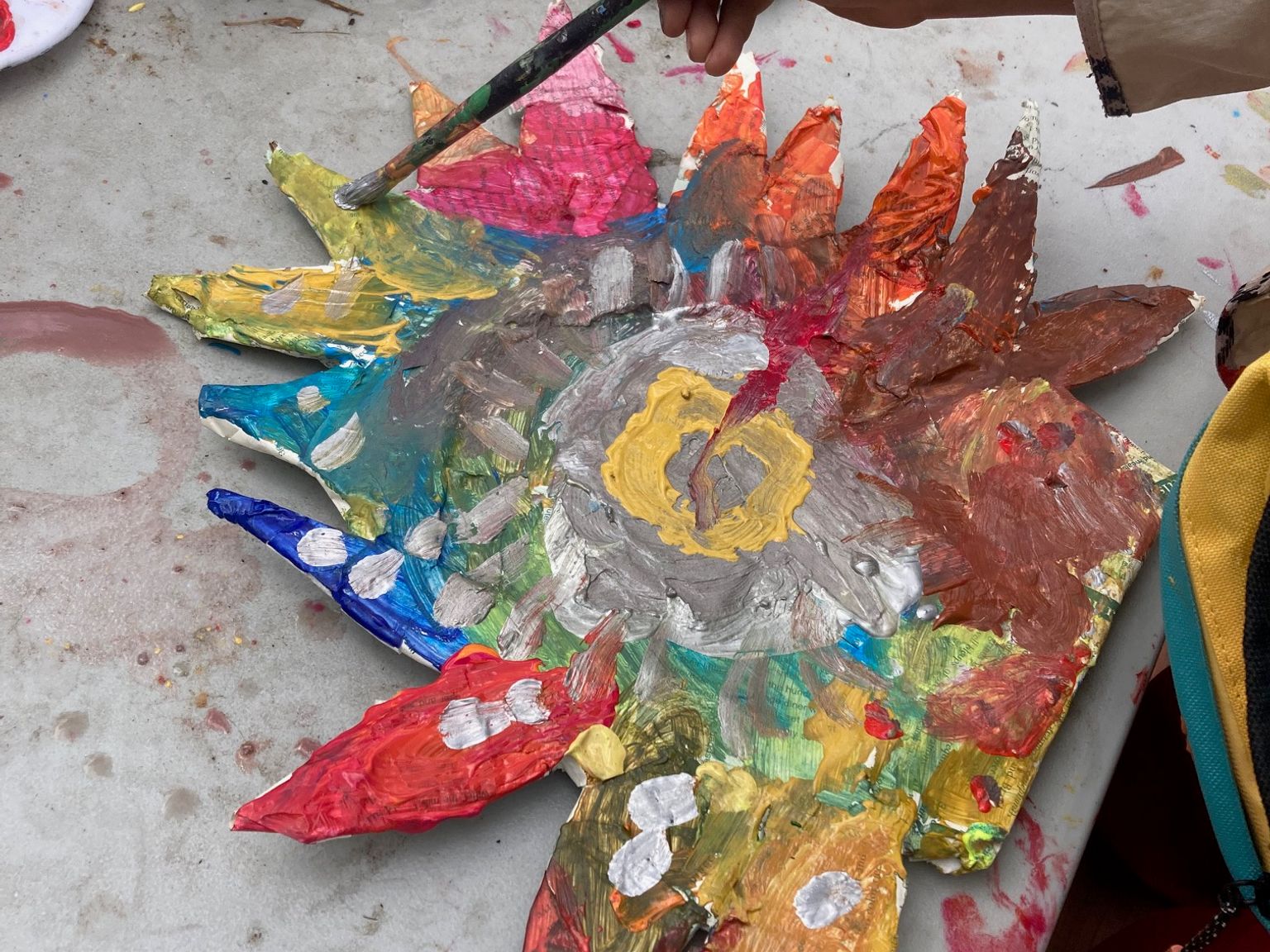 a child paints a colorful paper mache flower mask